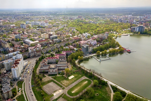 Vogelperspektive von Stadtsee unter grünen Bäumen und Stadtgebäuden in der Erholungsparkzone. Drohnenfotografie.