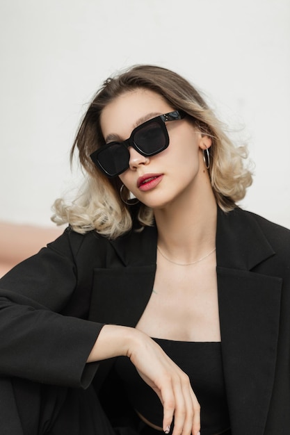 Vogue elegante Business Fashion Beauty Woman mit modischer Sonnenbrille in schwarzem Outfit mit Top und Blazer sitzt auf der Straße