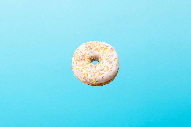 Volando en el aire donut con glaseado blanco sobre un azul. Panadería, concepto de cocción. Levitación