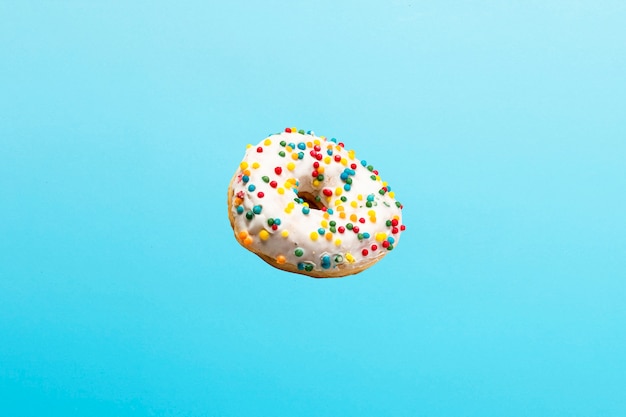 Volando en el aire donut con glaseado blanco sobre un azul. Panadería, concepto de cocción.