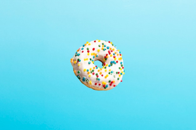 Volando en el aire donut con glaseado blanco sobre un azul. Panadería, concepto de cocción.