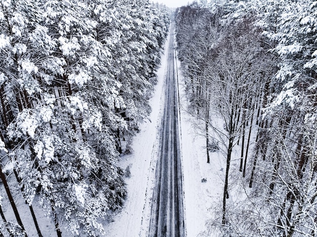 Volando sobre la carretera asfaltada y el bosque cubierto de nieve en invierno Polonia