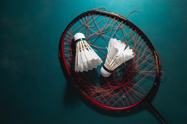 Volante de bádminton con raqueta de bádminton rompiendo cuerdas en el suelo de goma de la cancha