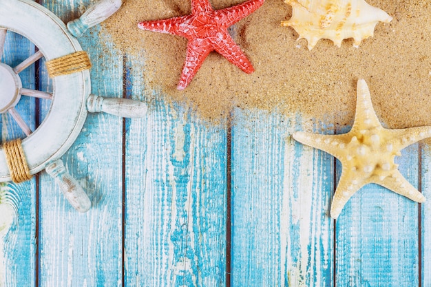 Volante decorativo con estrellas de mar, conchas marinas en la playa de arena y tablas de madera.
