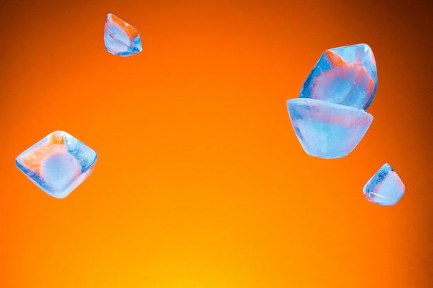 Volar piezas de fusión de hielo azul sobre un fondo naranja. Concepto de calor de verano