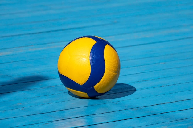 Voleibol amarillo en cancha de voleibol El piso es de madera y está cubierto con pintura azul