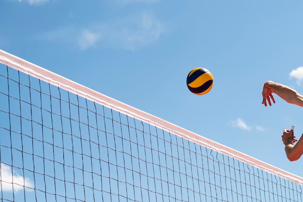Voleibol voando pelo ar com as mãos visíveis contra o fundo de um céu azul com nuvens