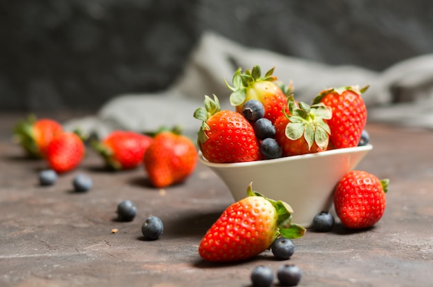 Voll von der keramischen Schüssel mit Blaubeeren und Erdbeeren auf der Steintabelle.