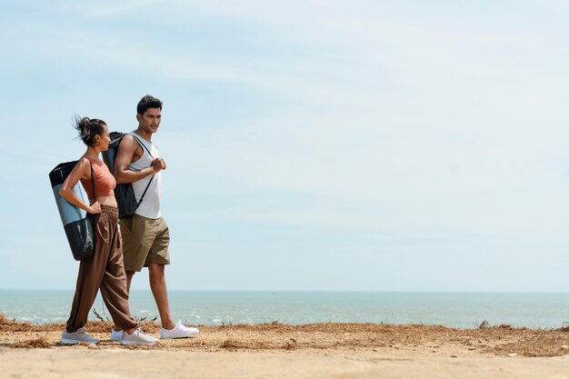 Vollbildpaar, das mit Yogamatten am Strand spazieren geht