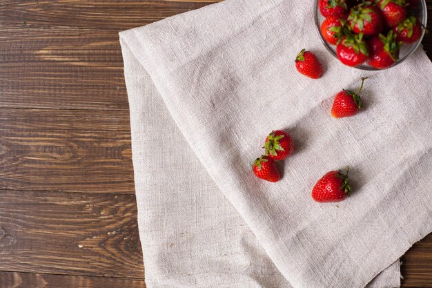 Volle Glasschüssel mit frischen reifen Erdbeeren und Küchentuch mit leckeren Erdbeeren drauf