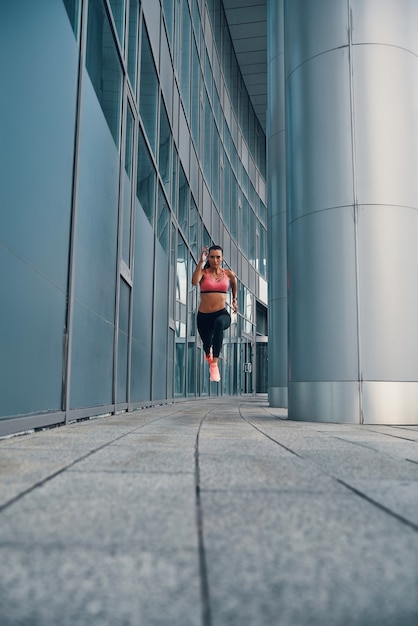 Volle Länge der attraktiven jungen Frau in Sportkleidung, die beim Training im Freien in einem Weitsprung schwebt