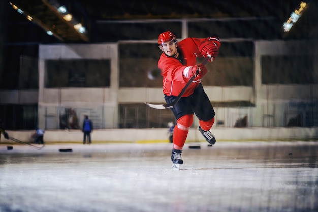 Volle Länge des Hockeyspielers, der auf Tor in der Eishalle schießt.