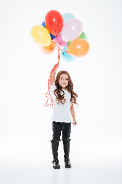 Volle Länge des lächelnden kleinen Mädchens, das bunte Luftballons hält