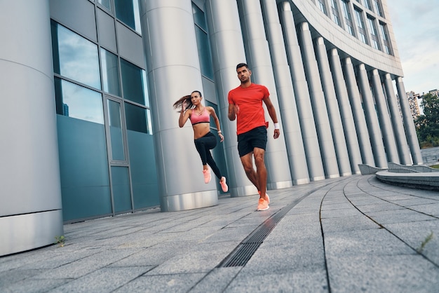 Volle Länge eines selbstbewussten, fitten Paares in Sportkleidung, das morgendliches Joggen beim Üben im Freien auf der Stadtstraße genießt