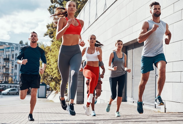 Volle Länge von Menschen in Sportkleidung beim Joggen auf dem Bürgersteig im Freien