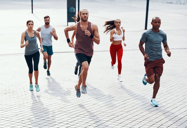 Volle Länge von Menschen in Sportkleidung beim Joggen auf dem Bürgersteig im Freien
