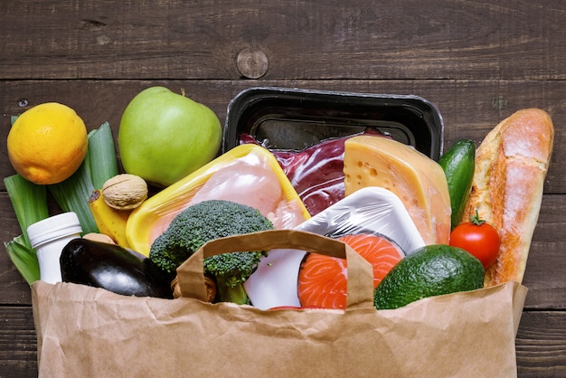 Volle Papiertüte mit verschiedenen gesunden Lebensmitteln auf weißem Holztisch. Obst, Gemüse, Fisch und Fleisch