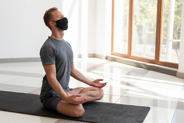 Voller Schuss junger Mann mit Gesichtsmaske, die Yoga drinnen praktiziert