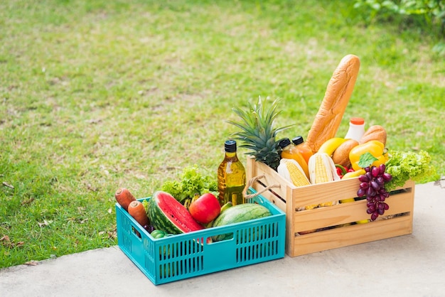 Volles frisches Gemüse und Obst in Kistenholzkiste, Ernte von Bio-Lebensmitteln auf dem Gartenplatz aus grünen Blättern, farbiger Hintergrund für Kopierraum, gesundes Essen