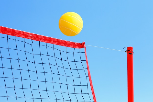 Volleyball auf dem Strand-, Netz- und Gelbenball auf Hintergrund des blauen Himmels.