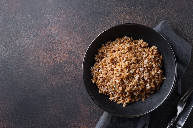 Vollkorn Dinkel Farro in Schüssel auf Braun. Draufsicht.