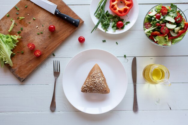 Vollkornbrot auf Teller und Salat auf weißem Holzhintergrund aus Tomaten, Gurken, Salat und rotem Pfeffer. Konzept für gesunde Ernährung.