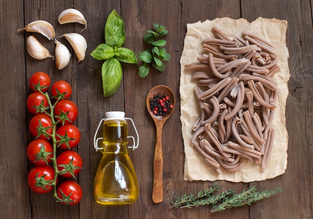 Vollkornnudeln, Gemüse, Kräuter und Olivenöl auf Holztischoberansicht