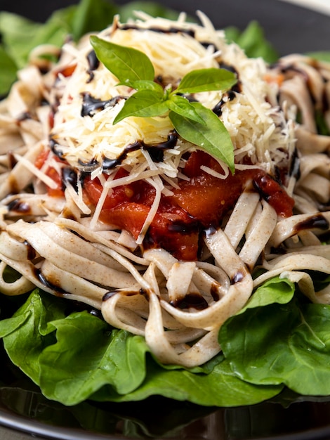 Vollkornnudeln mit Parmesankäse, grünen Blättern von Rucola, roter Sauce und Balsamico-Essig auf schwarzem Teller und weißem Marmorhintergrund