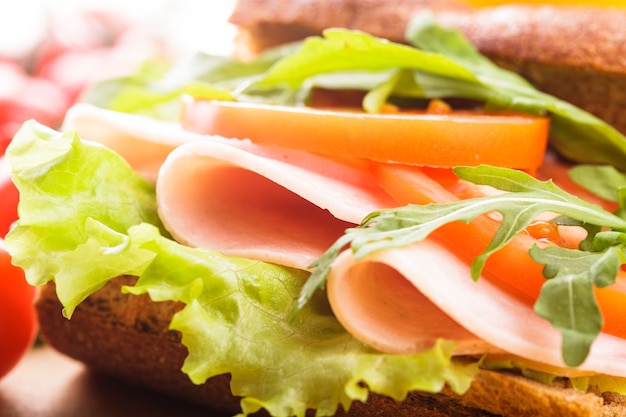 Vollkornsandwich mit Schinken, Tomate, Lattuce und Rucola mit einem Glas Orangensaft. Frühstück