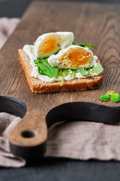 Vollkornsandwiches mit Guacamole, Rucola und Ei. Frühstück auf einem Holzbrett.