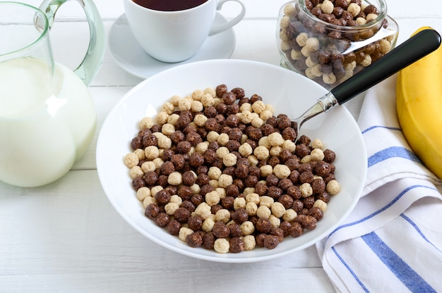 Vollkornschokolade und Milchbällchen, Obst, Tee und Milch auf weißer Holzoberfläche. Gesundes Müsli-Frühstück. Babyfrühstück. Baby essen. Ausgewogene Ernährung.