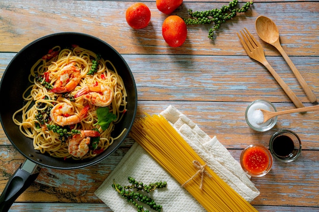 Vollkornspaghetti mit Garnelen in einer Pfanne auf blauem Schieferstein oder Betonhintergrund