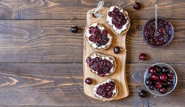 Vollkorntoast mit Ricotta und hausgemachter Süßkirschmarmelade auf Holzbrett und Hintergrund Kopierbereich