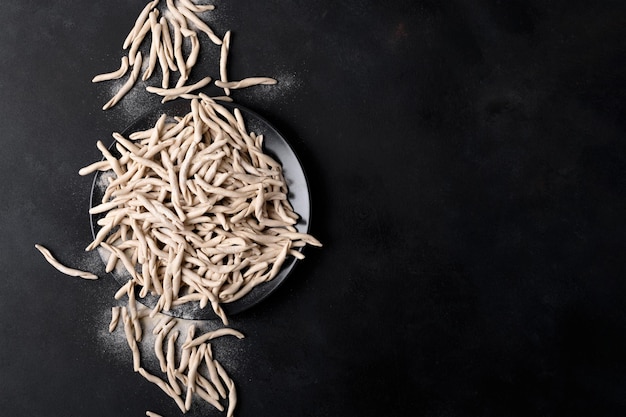 Vollkornweizen rohe apulische Pasta namens Pizzarieddi oder Maccaruni auf einem Teller auf schwarzem Tisch. Typisches Gericht der frischen Maccheroni von Apulien Salento Italien. Hintergrund der italienischen hausgemachten Pasta, Draufsicht, oben