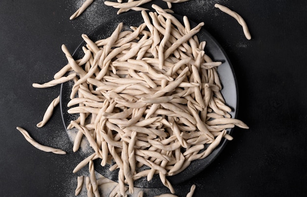 Vollkornweizen rohe apulische Pasta namens Pizzarieddi oder Maccaruni auf einem Teller auf schwarzem Tisch. Typisches Gericht der frischen Maccheroni von Apulien Salento Italien. Hintergrund der italienischen hausgemachten Pasta, Draufsicht, oben