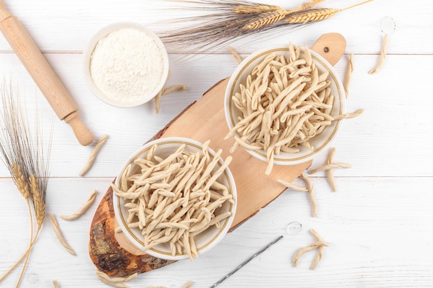 Vollkornweizen rohe apulische Pasta namens Pizzarieddi oder Maccaruni auf einer Keramikplatte auf weißem Holztisch