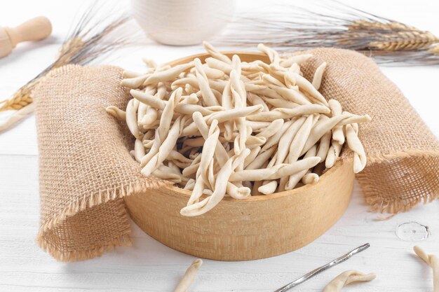 Vollkornweizen rohe apulische Pasta namens Pizzarieddi oder Maccaruni in einem Sieb auf weißem Holztisch