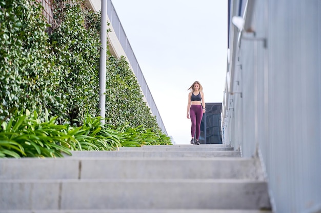 vollständige Ansicht einer Fitnessfrau in Sportbekleidung, die die Treppe hinunter geht