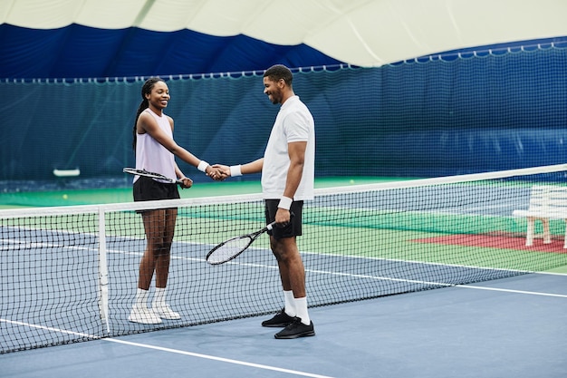 Vollständige Aufnahme von zwei Tennisspielern, die während des Spiels im Kopierraum des Hallenplatzes die Hände über das Netz schütteln