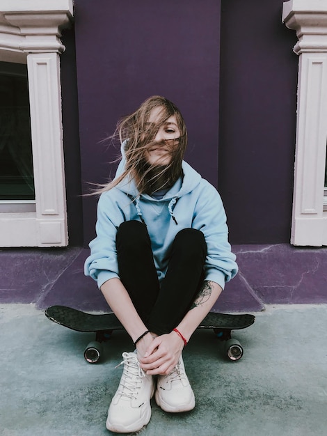 Vollständige Länge einer Frau, die auf einem Skateboard an der Wand sitzt