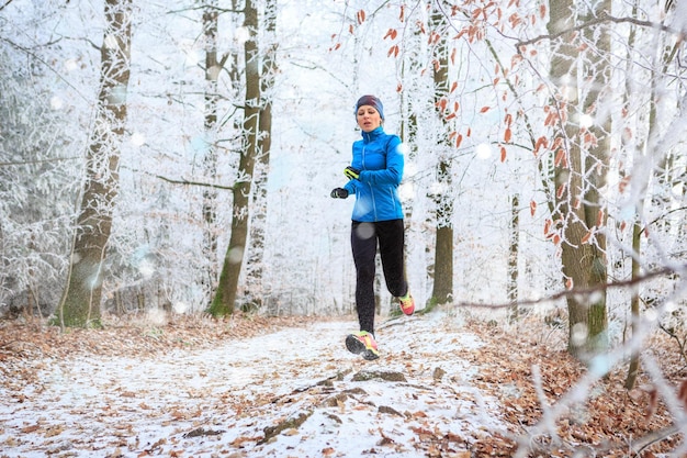 Vollständige Länge einer mittleren erwachsenen Frau, die im Winter auf einem Fußweg im Wald läuft