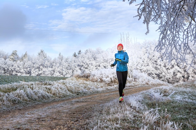 Vollständige Länge einer mittleren erwachsenen Frau, die im Winter auf einem Fußweg im Wald läuft