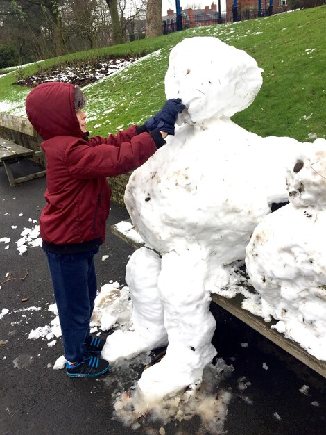 Foto vollständiger junge, der im park einen schneemann macht