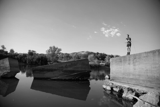 Vollständiger Mann, der am See gegen den Himmel springt