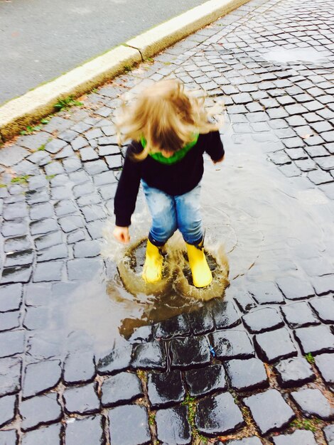 Foto vollständiges mädchen spielt in einer pfütze auf dem bürgersteig