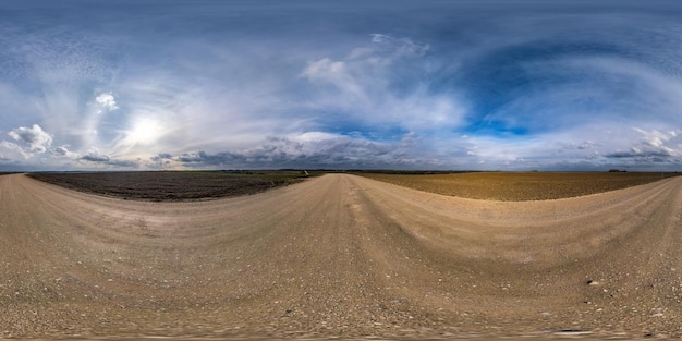 Vollständiges nahtloses sphärisches Hdri-Panorama 360-Grad-Winkelansicht auf Schotterstraße zwischen Feldern am Frühlingstag mit fantastischen Wolken in equirectangularer Projektion, bereit für VR-AR-Virtual-Reality-Inhalte