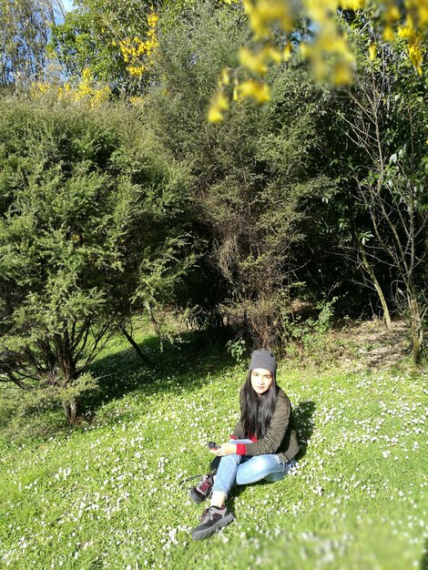 Foto vollständiges porträt einer jungen frau, die in einem park bei pflanzen sitzt