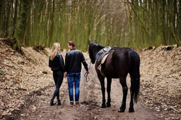 Volta do jovem casal elegante apaixonado andando com cavalo na floresta de outono