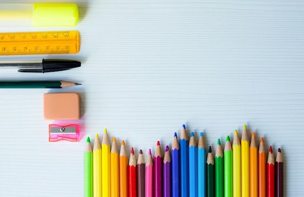 Volta para o quadro de escola com arco-íris de canetas coloridas e outros materiais escolares e fundo de madeira branco