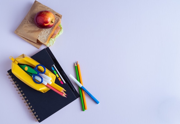 Voltar ao material escolar. Lápis, caderno e sanduíche em fundo roxo. Copie o espaço.